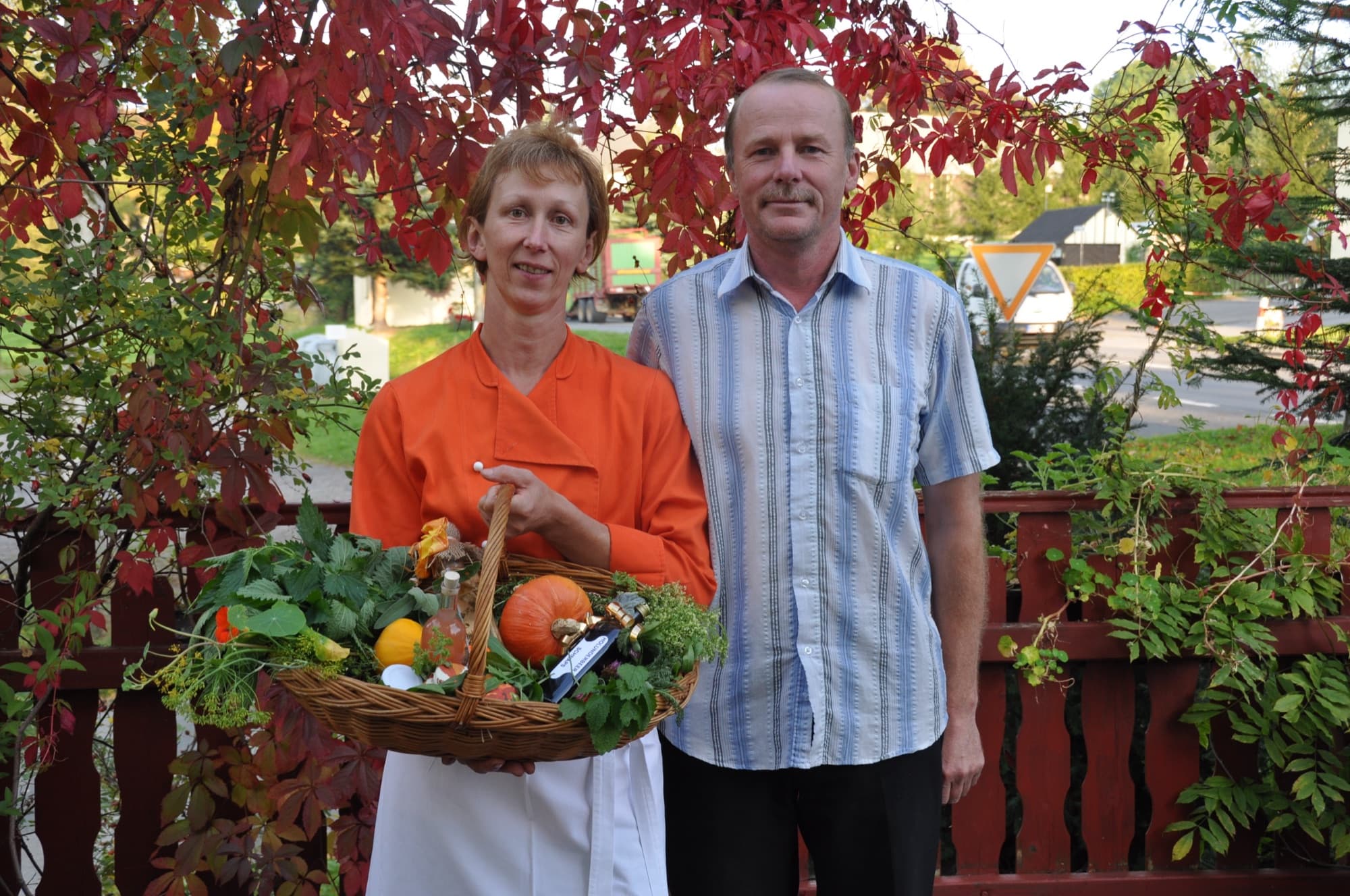 Petra und Roberto Martin mit einem Korb voller Kräuter und Kürbis vor Herbstlaub